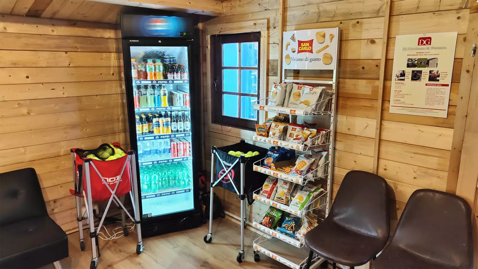 Frigorifero Pepsi con bevande e espositore San Carlo con snack salati al banco di un tipico circolo padel italiano: una decina di bevande sui ripiani, una decina di tipi di patatine, ambiente in legno